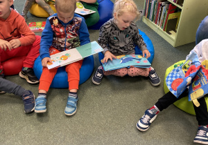 Dzieci siedzą na dywanie i wspólnie oglądają książki