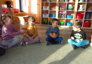 Dzieci siedzą na dywanie i ogladają dynie