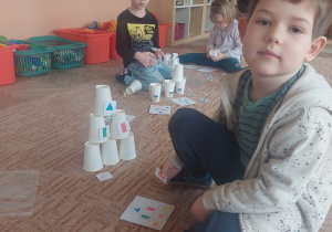 Chłopiec siedzi na dywanie i układa karty z figurami geometrycznymi