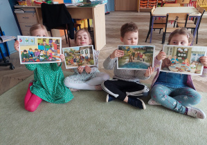 Czworo dzieci siedzi na dywanie z ilustracjami przedstawiającymi zwiastuny wiosny