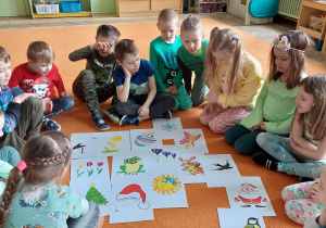 Dzieci siedza na dywanie przy ilustracjach z zwiastunami wiosny