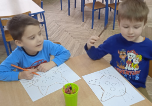 Dwóch chłopców siedzi przy stoliku i rysują na kartce papieru