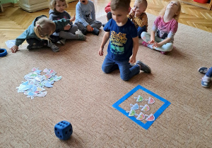 Dzieci siedzą na dywanie i układają obrazki do zbiorów
