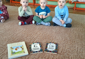 Dzieci siedzą na dywanie i rozmawiają o książkach