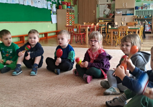 Dzieci siedzą na dywanie i trzymają w rękach grzechotki