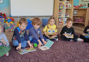 Grupa dzieci siedzi na dywanie i przegląda ilustracje w książkach