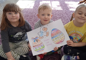 Troje dzieci prezentuje rysunek pisanki