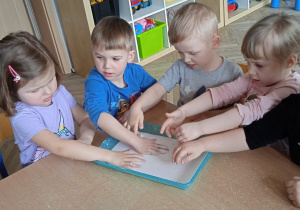 Grupa dzieci wklada ręcę do pojemnika z białym kolorem.