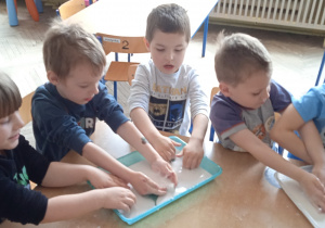 Grupa dzieci wkłada ręcę do masy plastycznej.