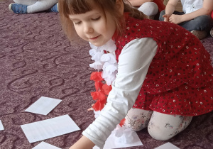 Dziewczynka układa na dywanie elementy papierowej flagi.
