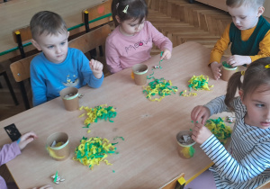 Grupa dzieci wykonuje prace wielkanocne przy stoliku.