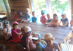 Dzieci siedzą przy drewnianej ławie.