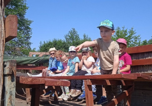 Grupa dzieci siedzi siedzi na drewnianej ławce.
