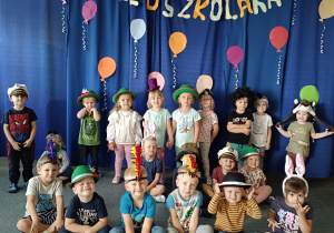 Grupa dzieci w kolorowych nakryciach głowy na tle dekoracji