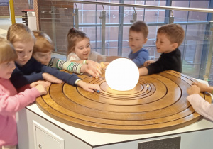 grupa dzieci przy świecącej kuli imitującej Słońce