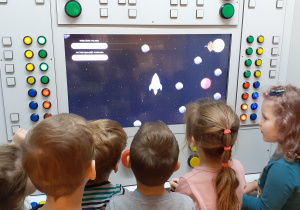 dzieci patrzą na ekran gry z rakietą i kometami
