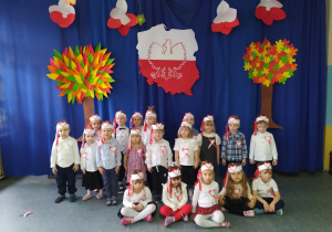 grupa dzieci odświętnie ubrane na tle dekoracji patriotycznej