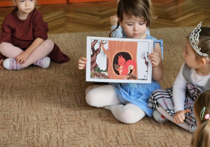 dziewczynka pokazuje obrazek z wiewiórką a po lewej stronie siedzi druga dziewcynka