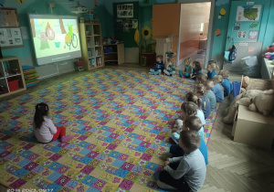 dzieci siedzą na dywanie i oglądaja film