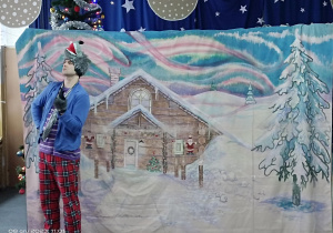 scenografia zimowa z domkiem i stojącym przed nim aktorem w przebraniu wilka
