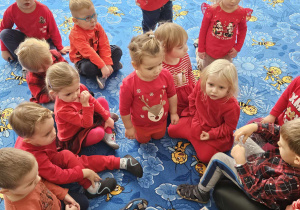 grupa dzieci ubrana na czerwono siedzi na dywanie