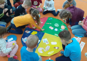 dzieci przyklejają obrazki na pomalowany w czterech kolorach duży owal
