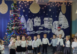 Dzieci w galowych strojach na tle świąteczno-zimowej dekoracji