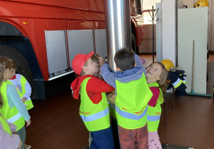 Dzieci stoją przy rurze, po której zjeżdżają strażacy