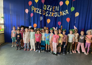 Grupa dzieci stoi na tle dekoracji Dzień Przedszkolaka