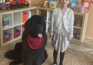 dziewczynka stoi obok czarnego psa
