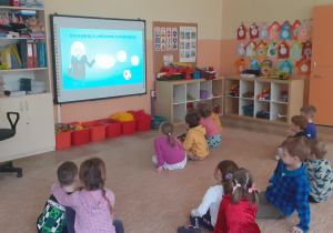 dzieci siedzą przed ekranem tablicy i oglądają film edukacyjny