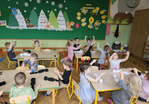 dzieci przy stole podnoszą do góry ręce z kolorowymi sznurkami