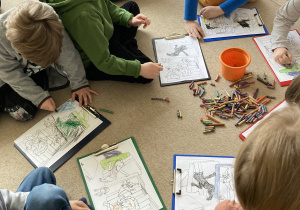 ilustracje rozłożone na dywanie, a dzieci kolorują
