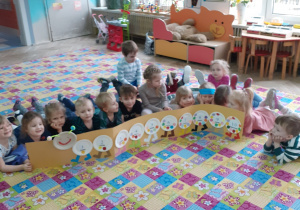 dzieci leżą na dywanie i prezentują gąsiennicę liczbową ułożoną z papierowych talerzyków