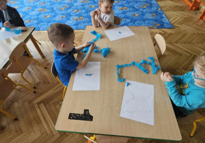 Dzieci zwijają niebieską bibułę przy stolikach
