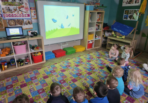 Dzieci siedzą przed ekranem wyświetlanego filmu