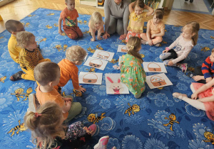 Dzieci na dywanie mają obrazki z koszyczkami, zajączkiem i marchewkami