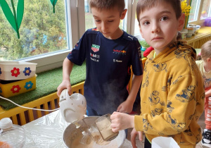 Jeden chłopiec miksuje a drugi wsypuje mąkę