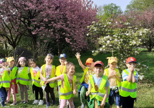 Grupa dzieci pozuje do zdjęcia na tle drzew kwitnącej wiśni