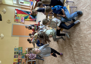 dziewczynka z marchewką w ręku porusza się dookoła grupy dzieci siedzących na krzesełkach