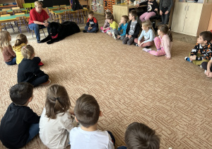 czarny pies leży na dywanie, wokół siedzą dzieci