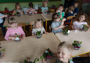 grupa dzieci prezentuje rośliny zasadzone w słojach