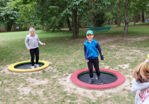 dwoje dzieci stoi na małych trampolinach