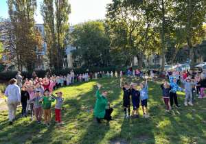 dzieci ze wszystkich grup stoją w kolę i machają
