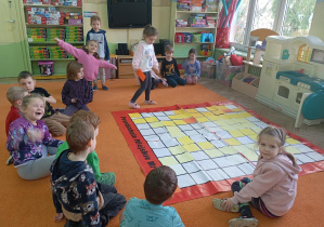 Dziewczynka idzie w stronę maty z kolorową kartką a reszta przygląda się